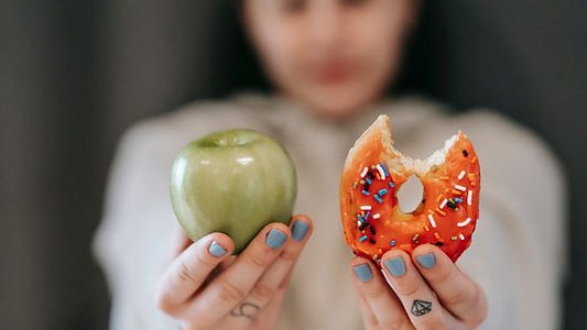 Hand hält Apfel und abgebissenen Donut