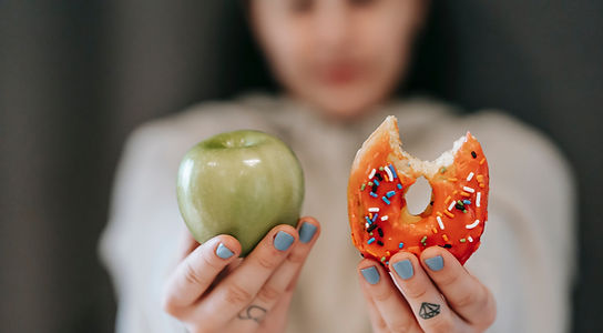 Hand hält Apfel und abgebissenen Donut